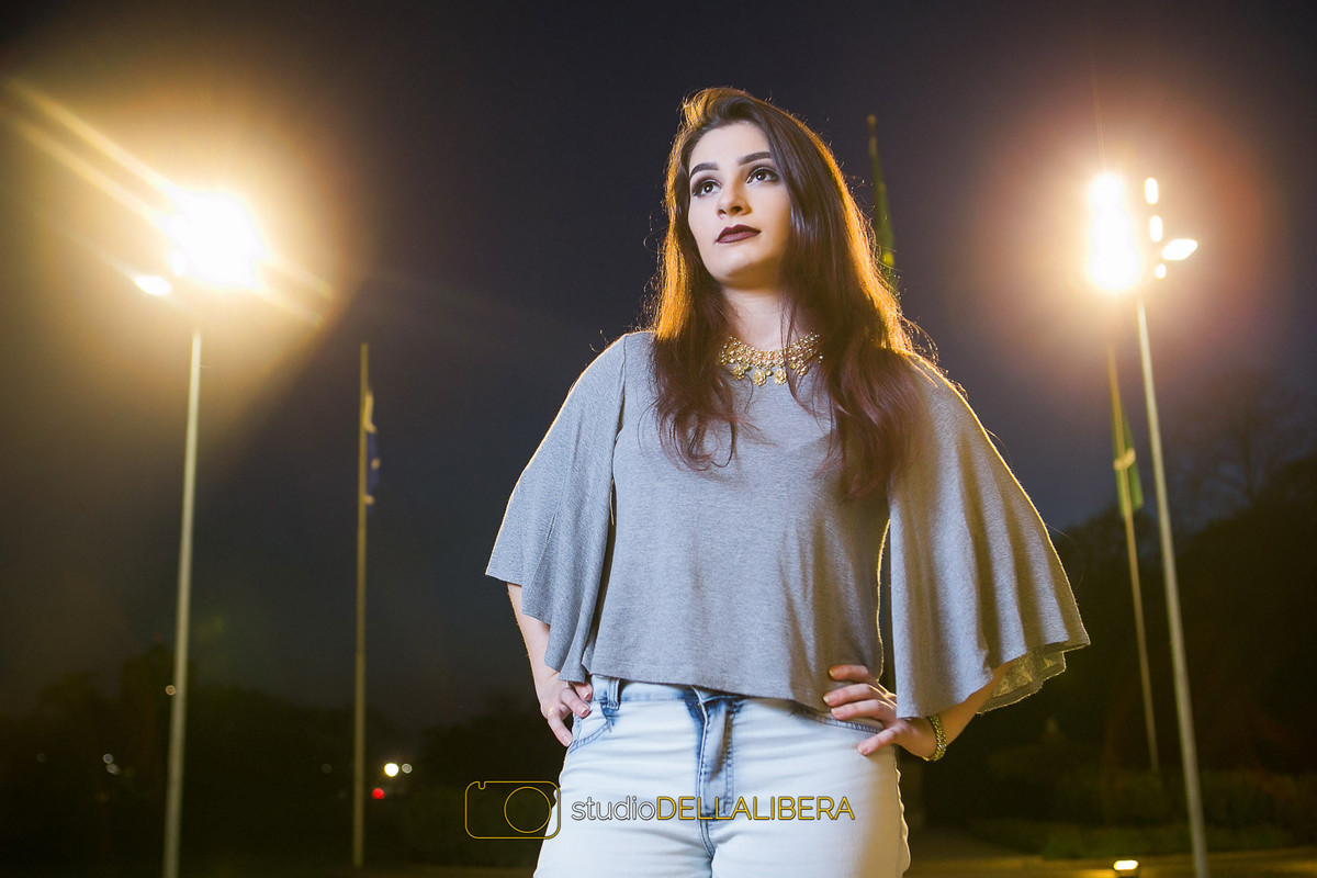 alanis modelando no final do dia com céu azul olofotes de fundo e a bandeira brasileira na sessão fotográfica de família feita na Esalq em SP