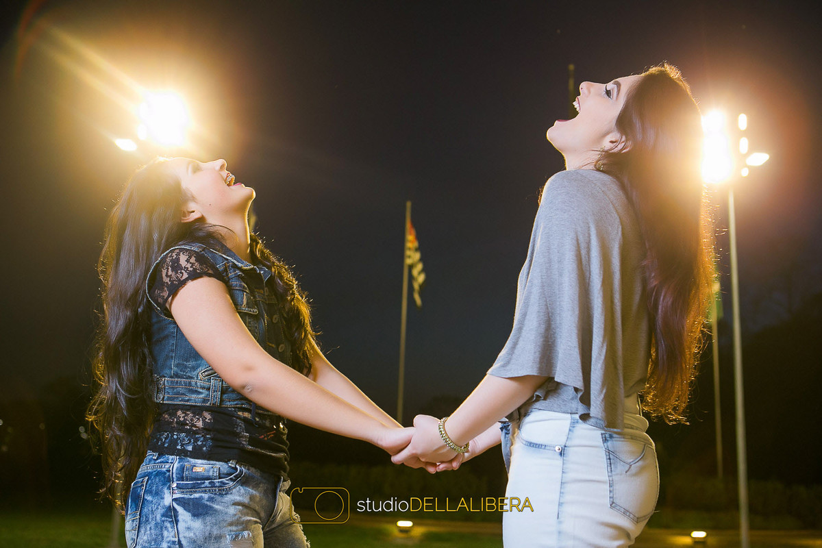 Irmãs de mãos dadas com uma gragalhada na sessão fotografica de família feita no final do dia em Piracicaba SP no parque da Esalq