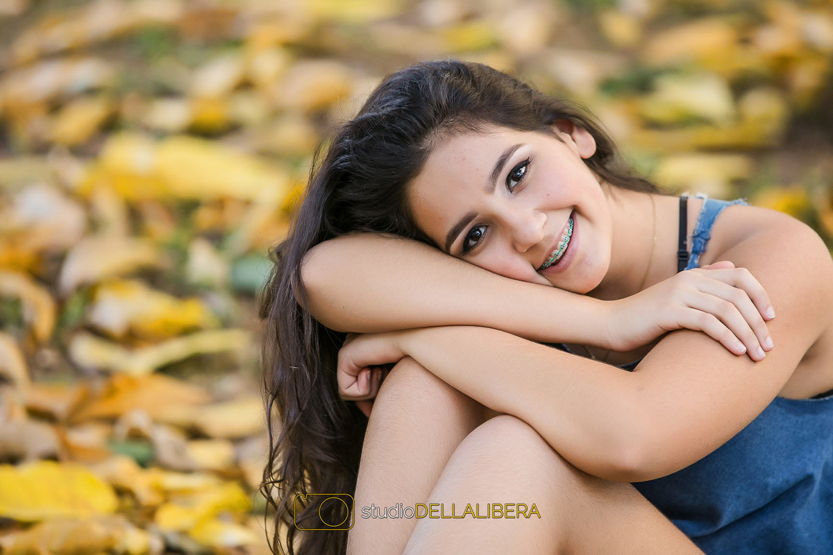 Modelo Laura com a cebeça debruçada nos braços com fundo cheio de folhas caidas