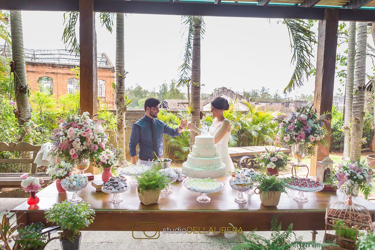 Casal na mesa de Bolo no Salão de festas do monte alegre com mesa decorada com flores do campo e noivos fazendo o brinde com champagnhe
