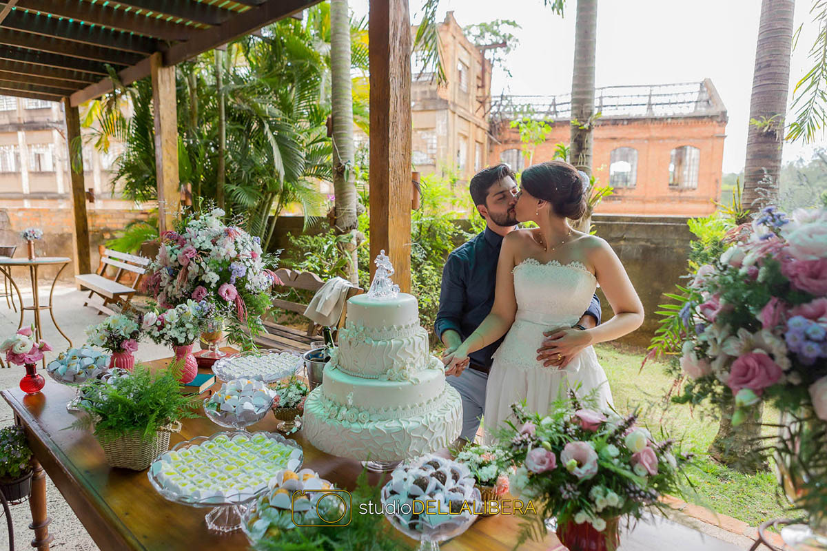 Beijo dos noivos no corte do bolo no salão de festas do Monte Alegre com mesa decorada e bolo de quatro andares