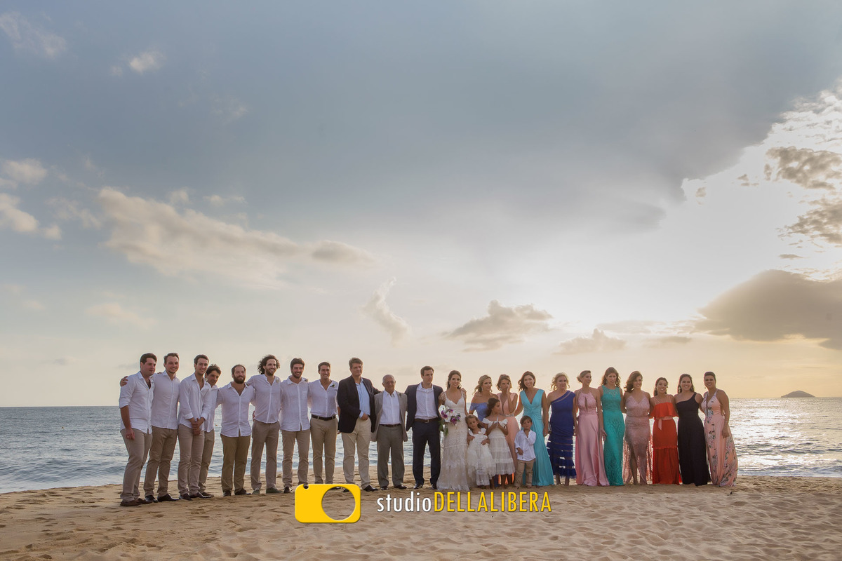 Padrinhos após a ceririmônia na areia da praia com a praia ao fundo céu se pondo , sendo padrinhos de um lado madrinhas de outro