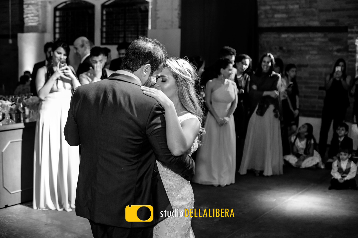 Noivos dançando a tradicional valsa, com a foto em PB feita pelo fotografo de casamento Wilson Della Libera Junior, os noivos bem Juntinho com os padrinhos e pagens ao fundo assistindo a dança do casal