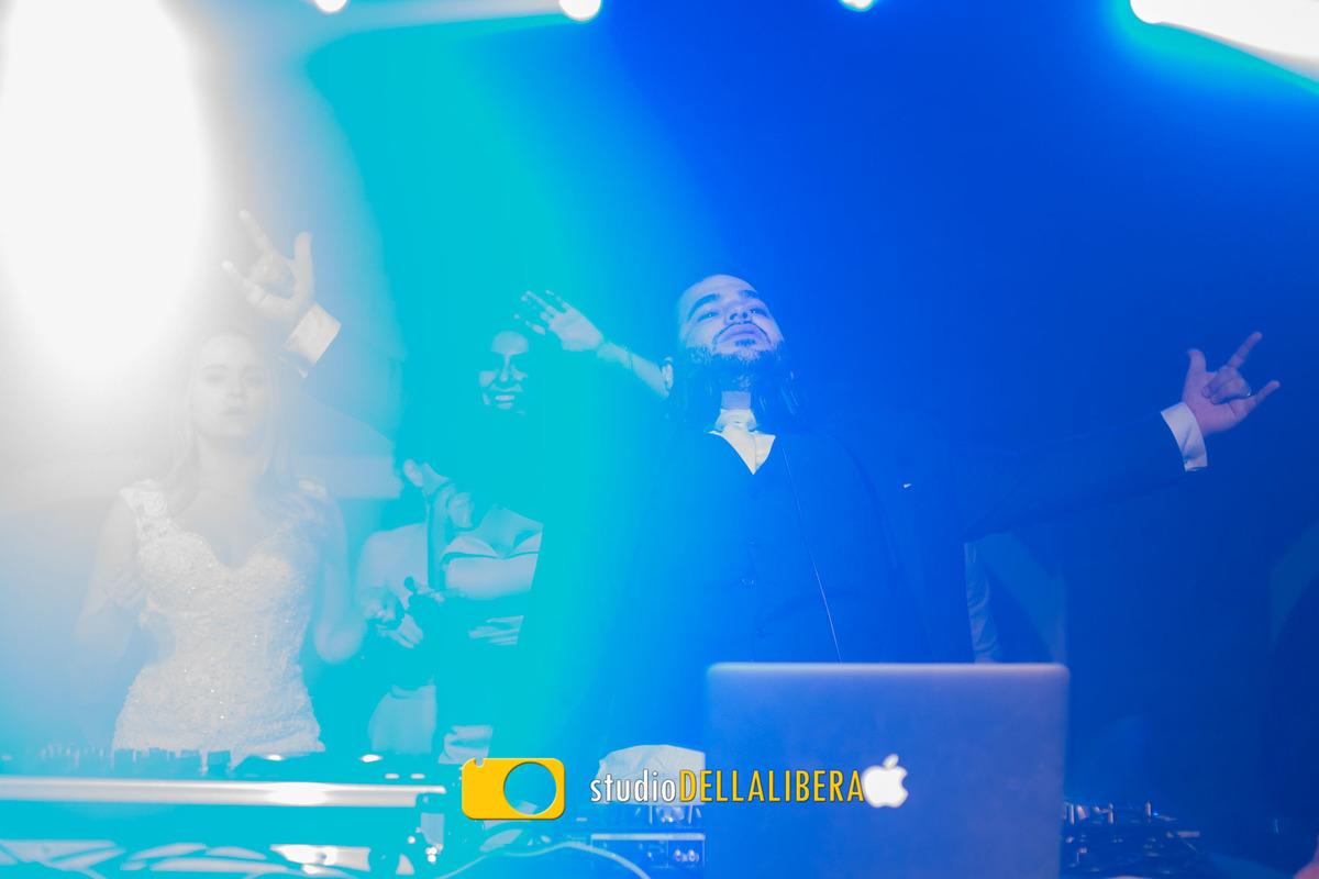 Noivo agitando a festa, sendo o DJ da festa de seu próprio casamento com a noiva atrás 