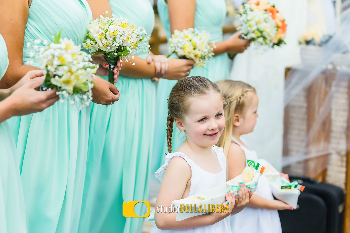 Madrinhas segurando buque vestidas com vestido verde com as duas daminhas na frente com vestidos brancos segurando as alianças 