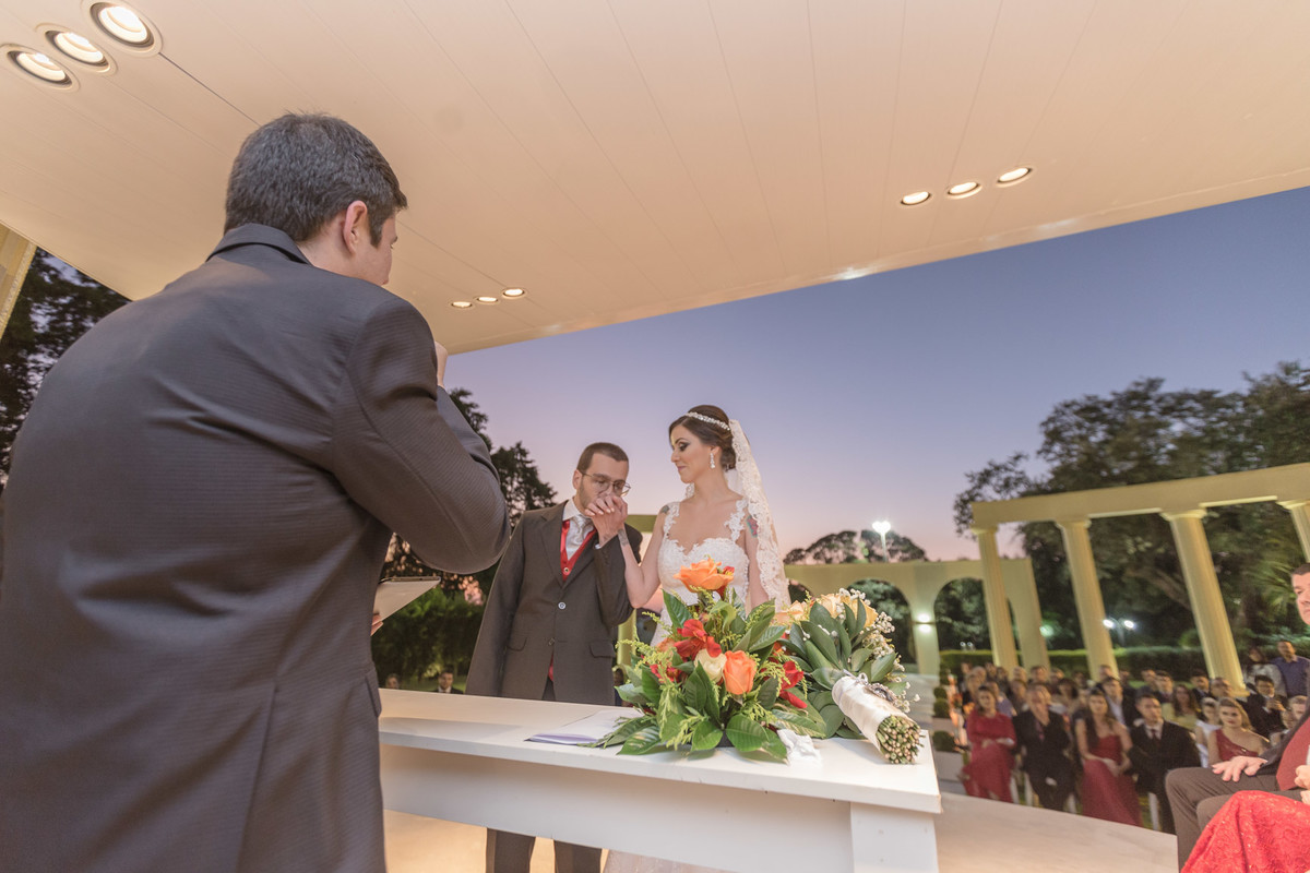 Noivos no altar e noivo beijando a mão da noiva e seu buque descansando na mesa em frente a eles