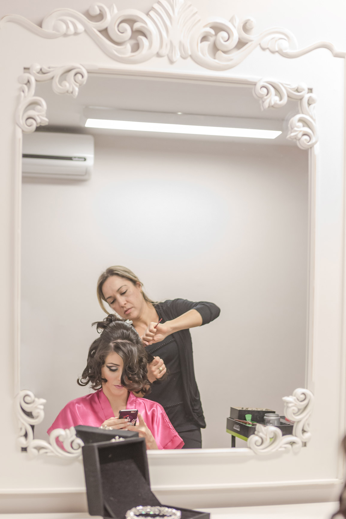 Noiva no making of mexendo no celular enquanto arrumam seu cabelo