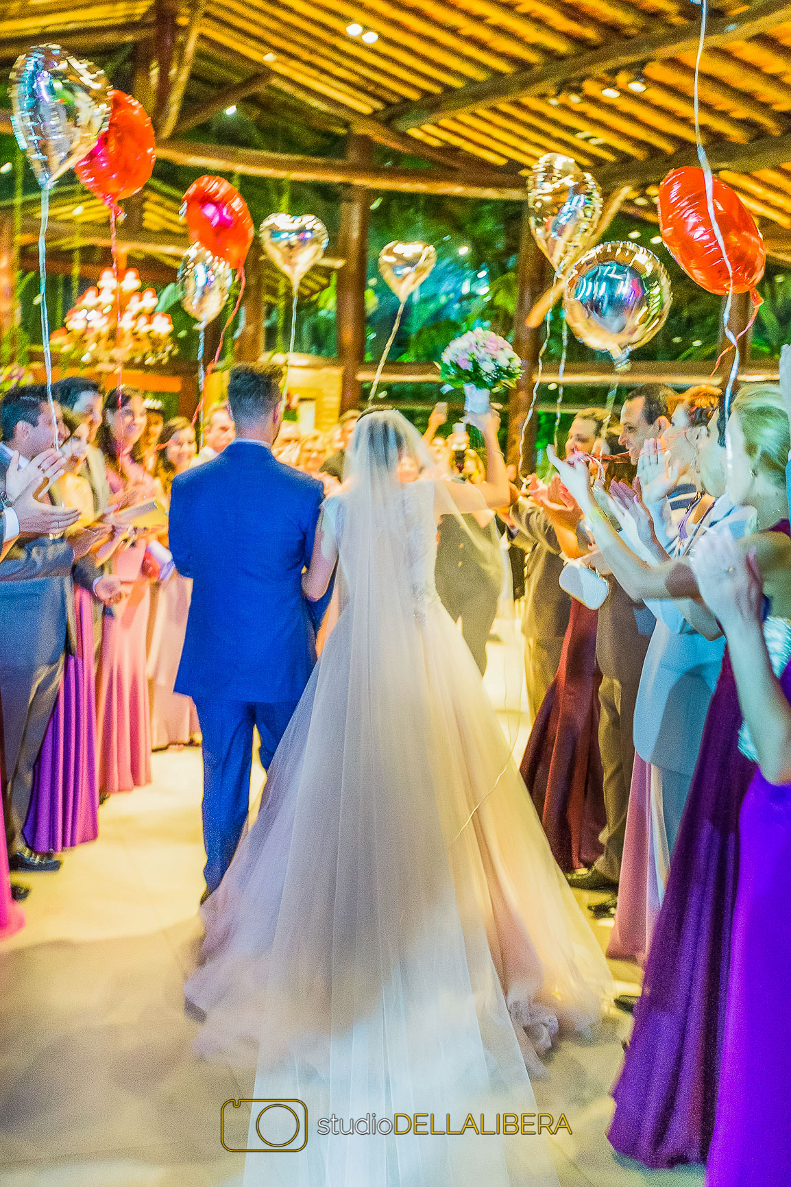 Noivos chegando no salão de festa Madero com padrinhos segurando balões cinza e vermelho em formato de coração