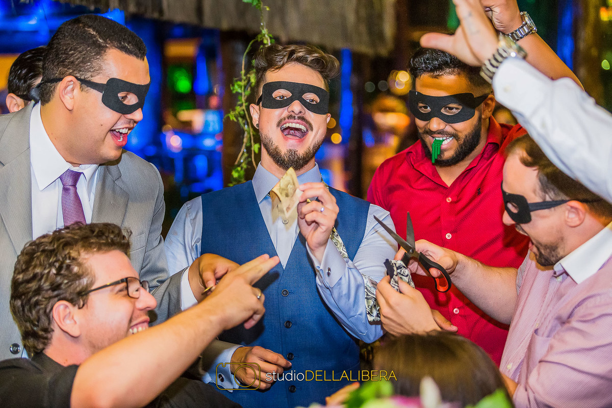 Everton com mascara segurando uma nota de dinheiro e convidado cortando a gravata dele