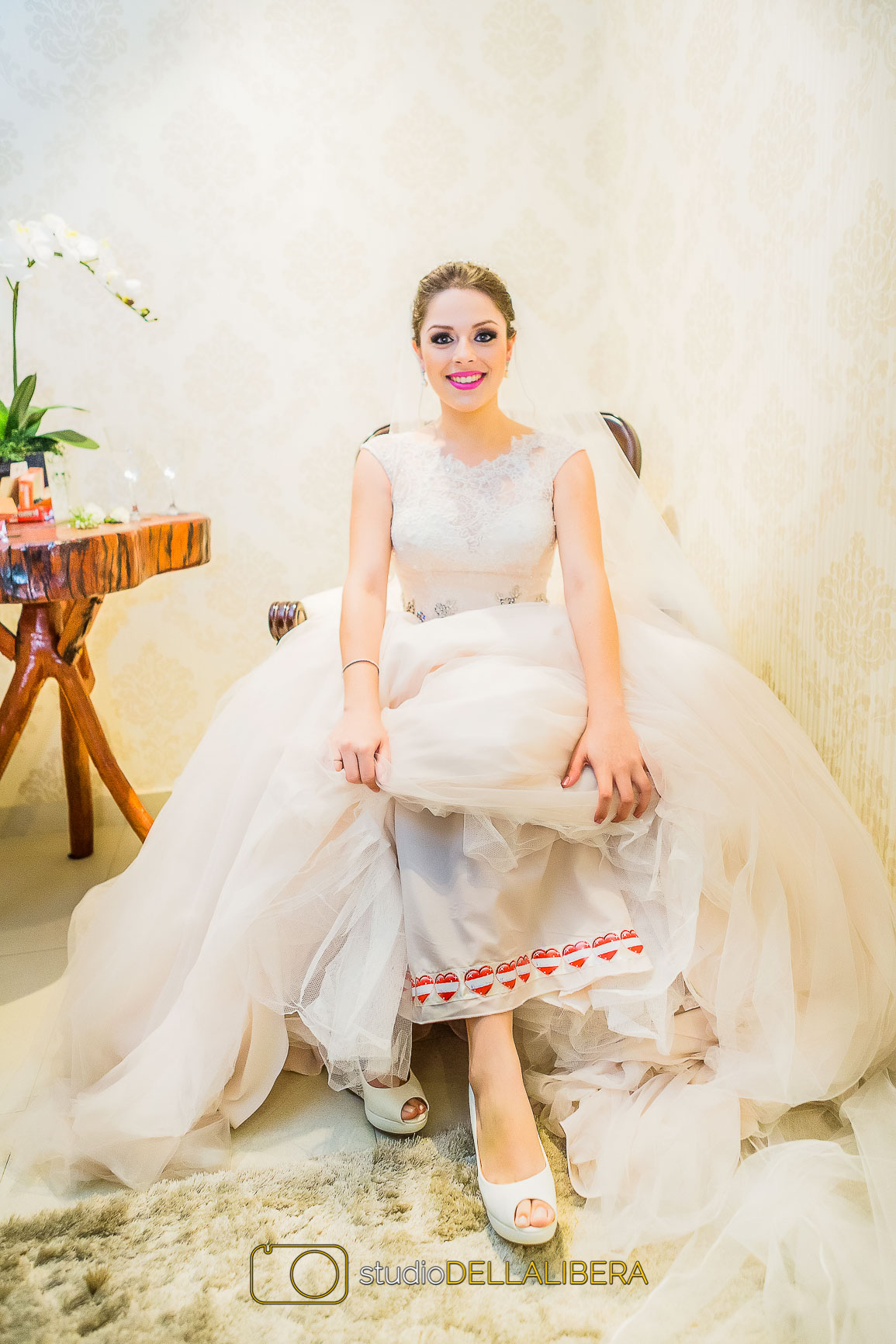 Noiva mostrando nomes de convidadas solteiras na barra do vestido sentada numa cadeira