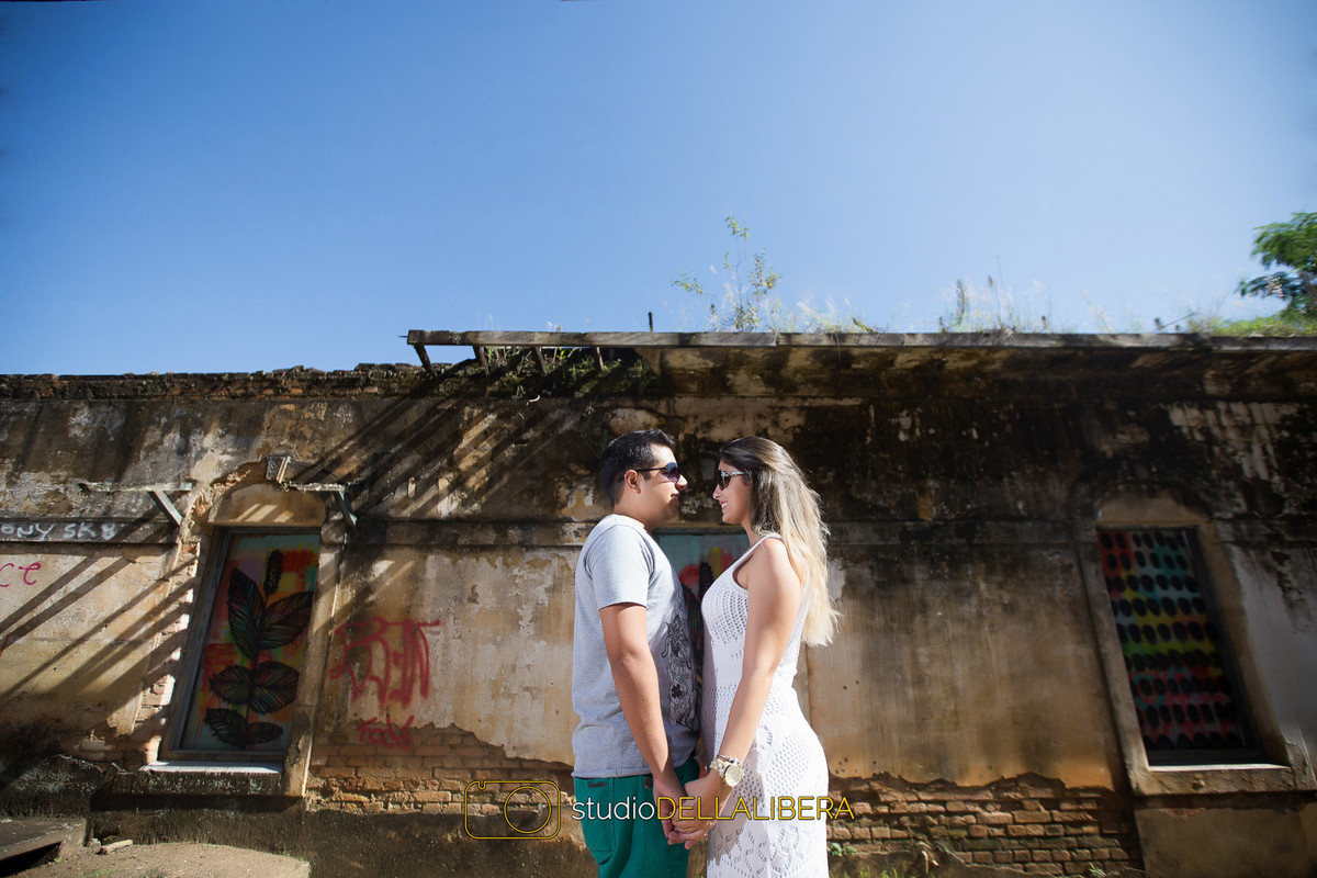 Noivos de frente um para o outro de óculos escuro e casa abandonada ao fundo