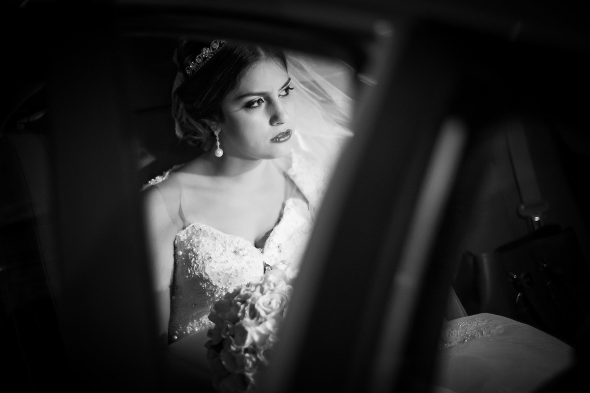 Noiva sentada pronta no carro olhando para o lado segurando seu buque