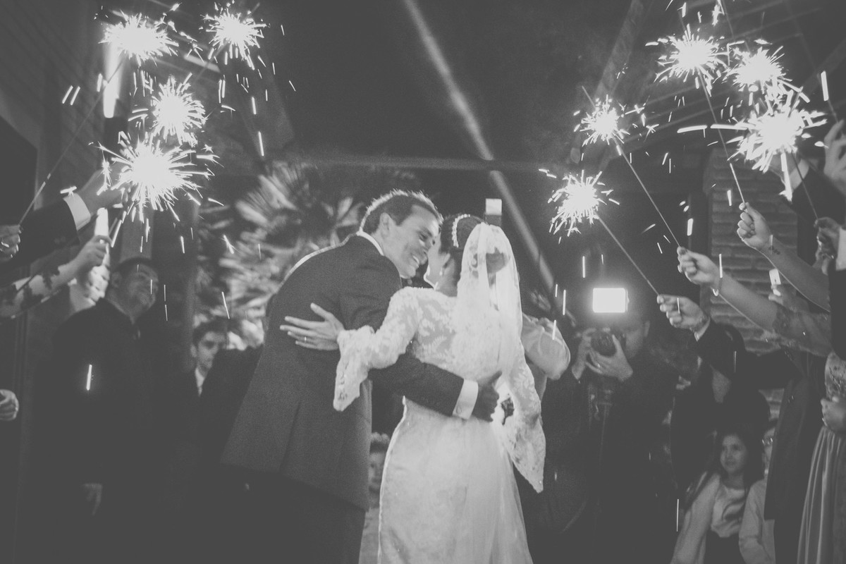 Noivo segurando noiva no corredor de saida com fogos de artificios  costas se beijando