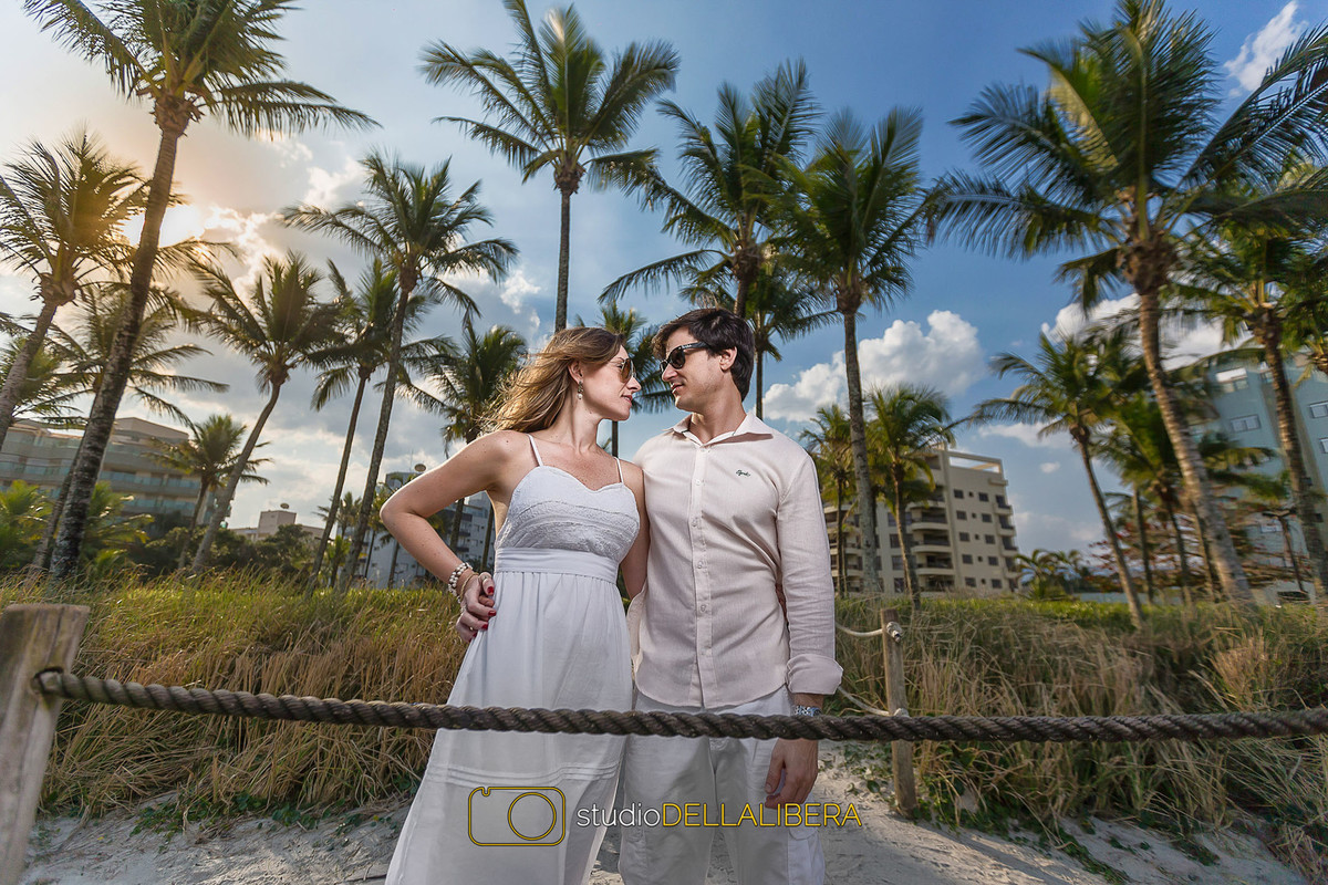 um olhar apaixonado dos noivos proxímo ao pier, com coqueiros de fundo um lindo céu azul