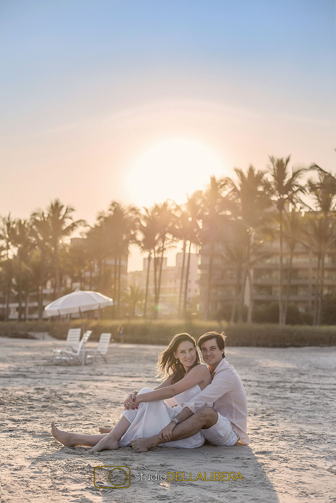 Por-do-sol fantastico na sessão pré casamento em Bertigo, com os noivos sentados na areia coqueiros ao fundo e o sol se pondo