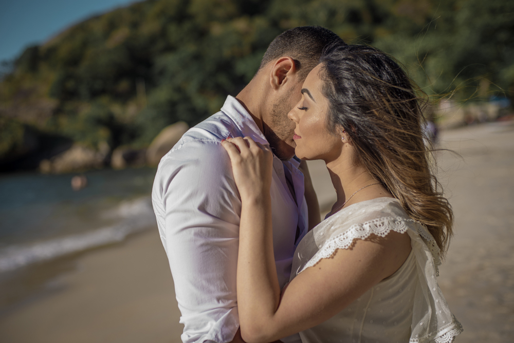 Melhor fotógrafo Nossa Casa Estúdio ensaio fotográfico profissional de casal na cidade de Niterói Rio de janeiro para pré wedding e casamento na praia de adão e eva ao por do sol na areia e mar com noivos/namorados vestidos de branco. Maquiagem noiva