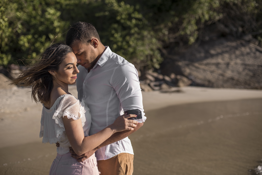 Melhor fotógrafo Nossa Casa Estúdio ensaio fotográfico profissional de casal na cidade de Niterói Rio de janeiro para pré wedding e casamento na praia de adão e eva ao por do sol na areia e mar com noivos/namorados vestidos de branco. Maquiagem noiva
