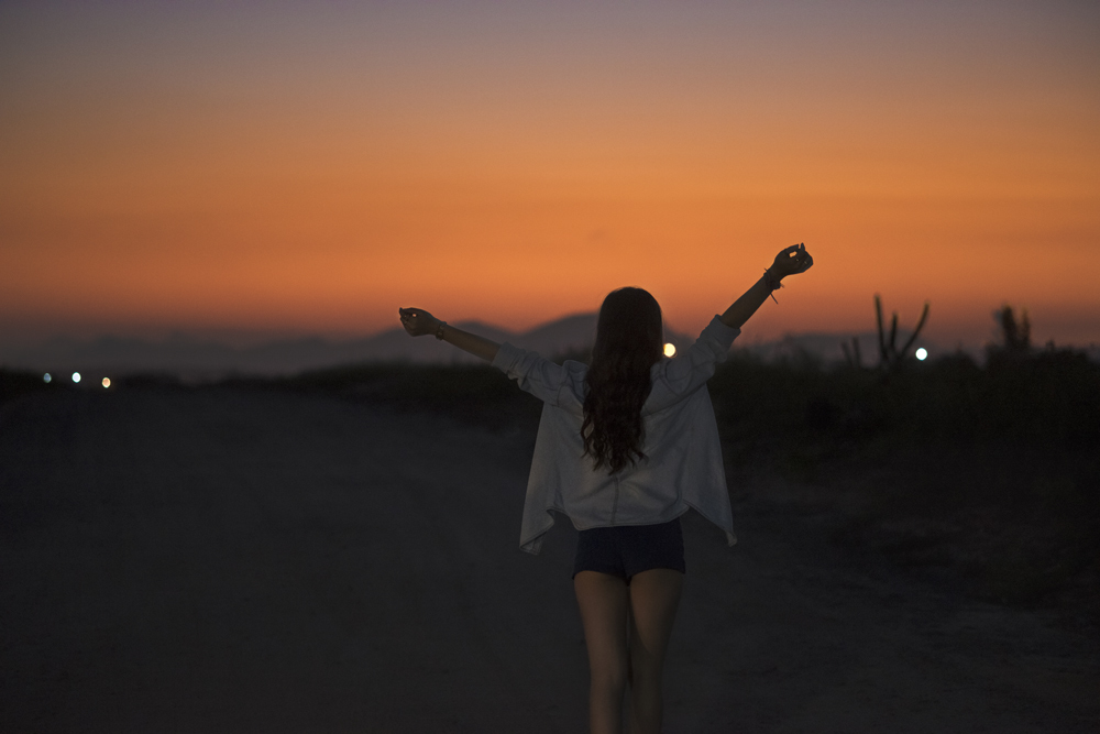 Ensaio fotográfico profissional de 15 anos na praia e no campo ao ar livre. Debutante de roupa e florida com tiara de flores na cabeça ao por do Sol, sorrindo. Festa Editorial Moda Revista Teen Adolescente Nossa Casa Estúdio Niterói Rio de Janeiro