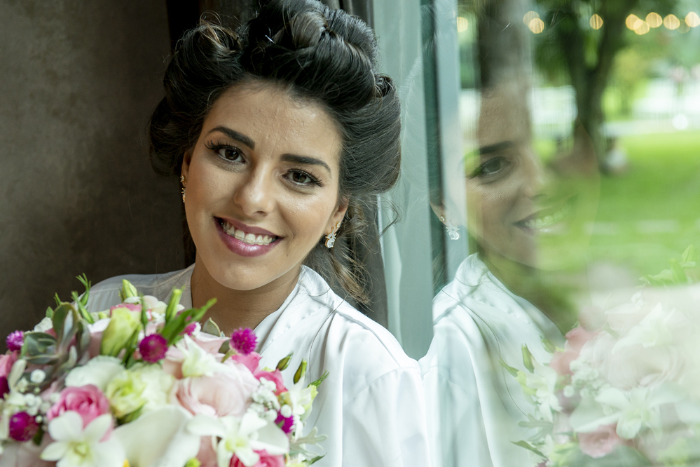Fotográfo de casamento em Niterói Rio de Janeiro Maricá no recanto dos coqueiros noiva se maquiando com maquiadora em making of com vestido branco antes da cerimônia e festa com Nossa Casa Estúdio maquiagem da noiva batom cores no espelho Buquê de flores