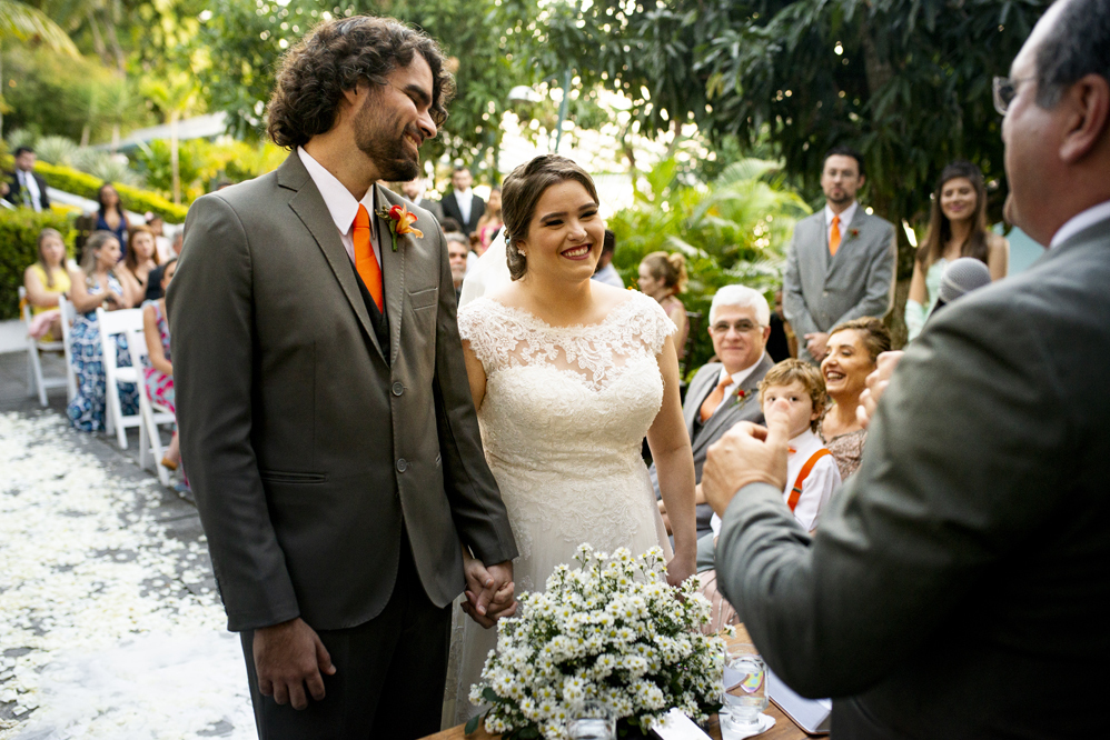 Nossa Casa Estúdio Fotografia de casamento em Niterói Rio de Janeiro Búzios Cabo Frio Hotel Atlântico Búzios noiva em cerimônia de casamento com noivo de gravata laranja  com vestido branco no por do Sol frente  mar para a praia com decoração rústica