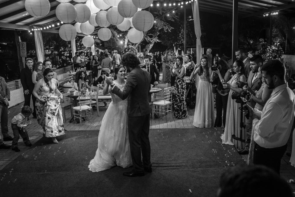 Nossa Casa Estúdio Fotografia profissional de casamento em Niterói Búzios Cabo Frio Rio de Janeiro em Hotel Atlântico Búzios casal de noivos dançando com vestido branco e terno com padrinhos madrinhas e convidados assistindo em festa na pista de dança