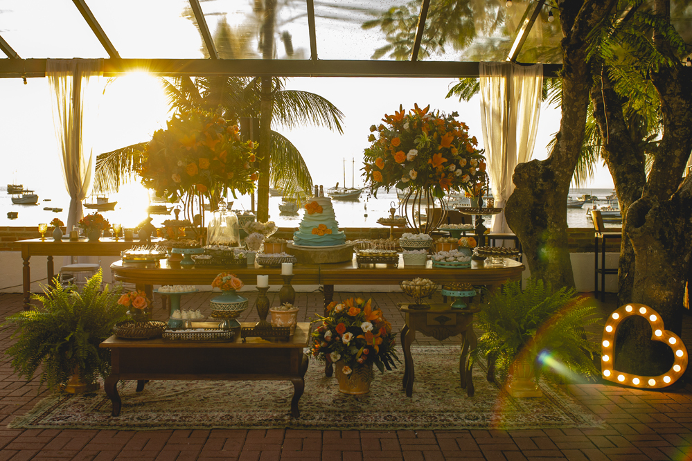 Nossa Casa Estúdio Fotografia de casamento profissional em Búzios Niterói Rio de Janeiro Decoração Rústica em festa no Hotel Atlântico Búzios para convidados casal de noivos com dicas e tendências a beira mar de dia no por do Sol laranja e docinhos