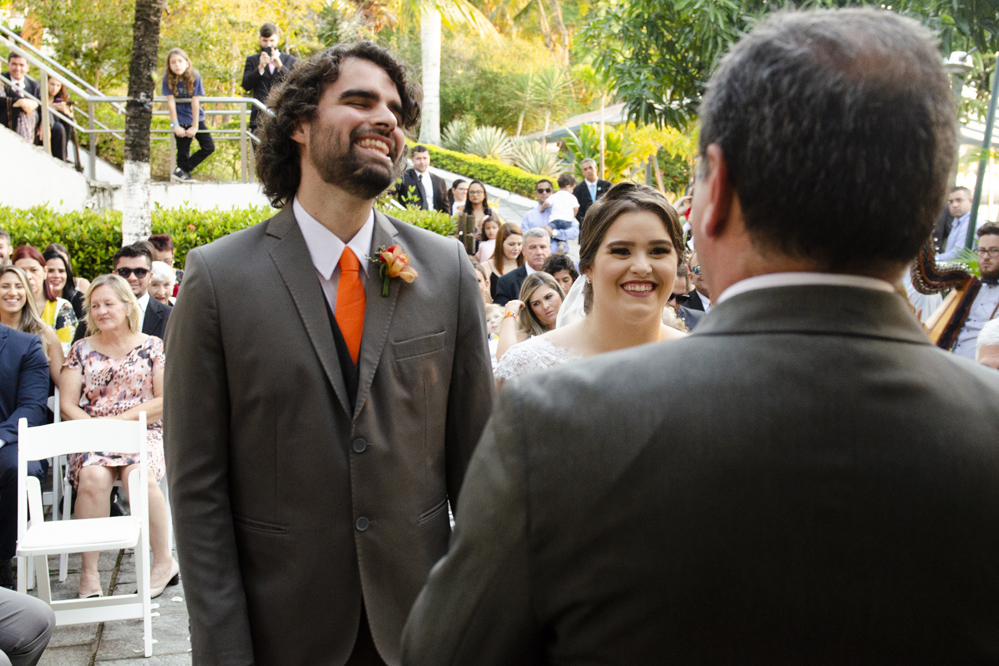 Nossa Casa Estúdio Fotografia de casamento em Niterói Rio de Janeiro Búzios Cabo Frio Hotel Atlântico Búzios noiva em cerimônia de casamento com noivo de gravata laranja  com vestido branco no por do Sol frente  mar para a praia com decoração rústica