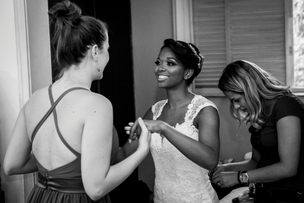 Noiva em making of com as amigas em fotografia preta e branca tirada por Gilson Freitas fotógrafo de casamentos profissional em Niterói e Rio de Janeiro  no making of madrinhas se preparando para a cerimônia e festa com vestido branco todas olhando 