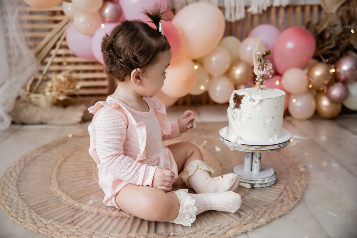 Bebe cenário smash the cake boho chic roupinha rosa comendo bolo bagunça com a mao olhando para o bolo