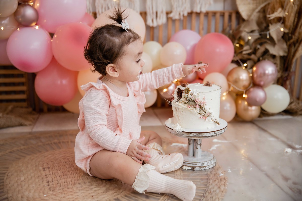 Bebe cenário smash the cake boho chic roupinha rosa comendo bolo bagunça com a mao olhando para o bolo mexendo no bolo