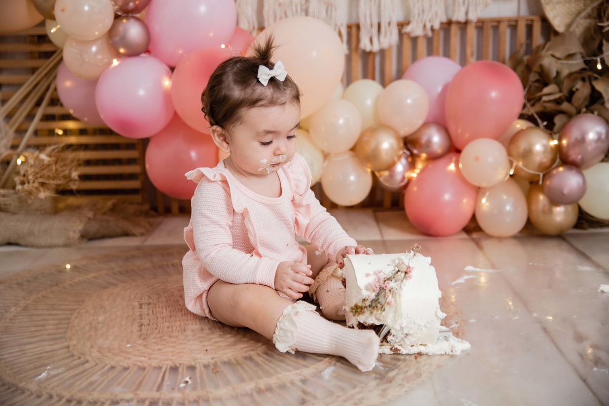 Bebe cenário smash the cake boho chic roupinha rosa comendo bolo bagunça com a mao olhando para o bolo jogou bolo chao