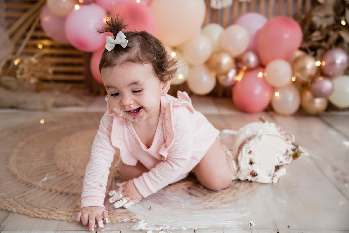 Bebe cenário smash the cake boho chic roupinha rosa comendo bolo bagunça com a mao olhando para o bolo fugindo