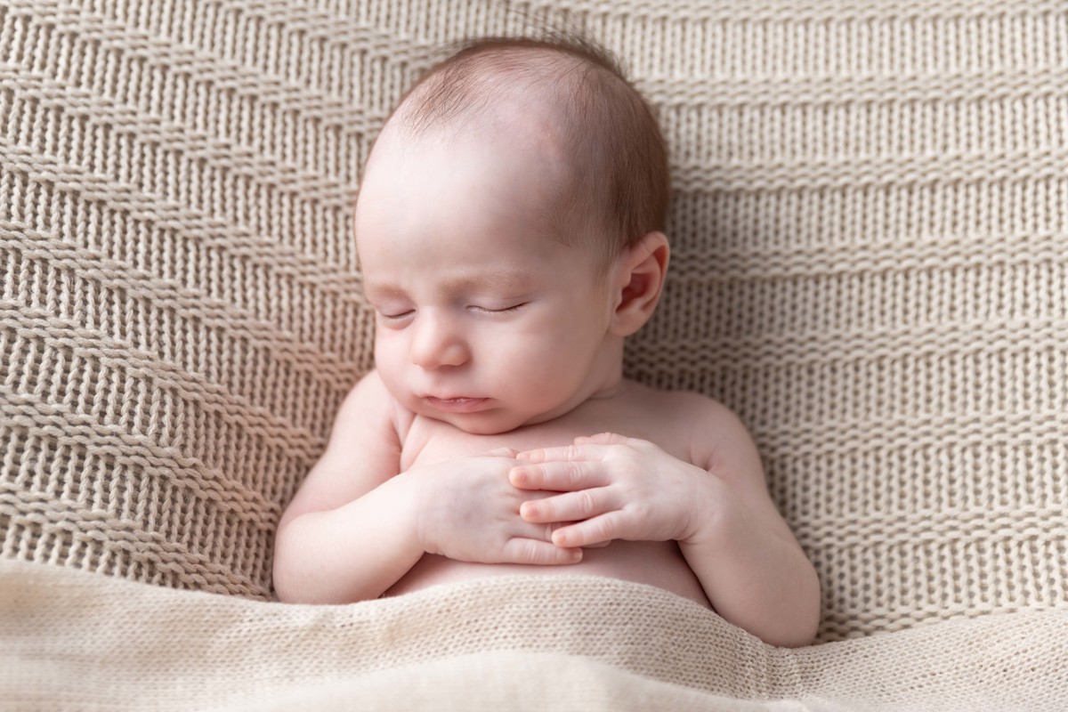 bebe deitado com mão de na barriguinha no pufe