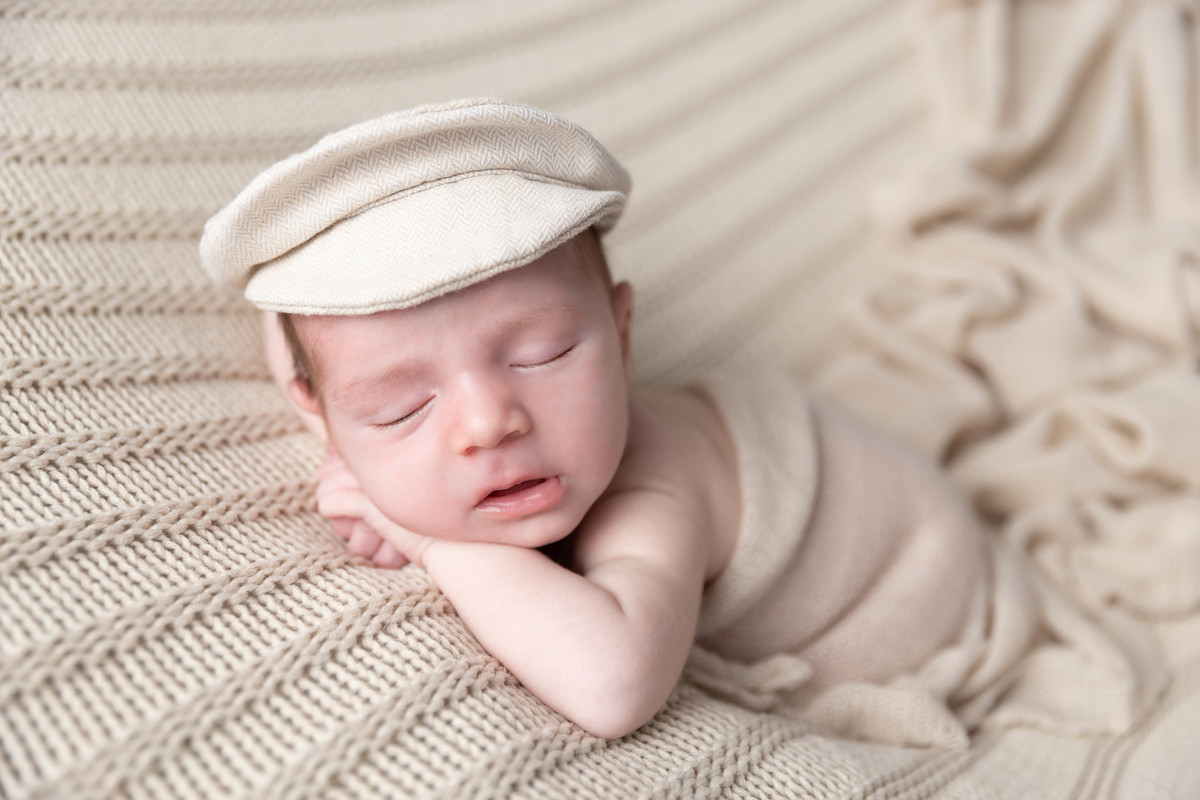 bebe deitado com mão no queixinho no pufe com boina