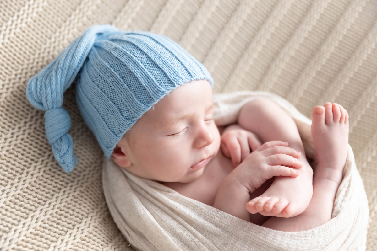 bebe deitado com mão no pézinho  no pufe com toquinha azul