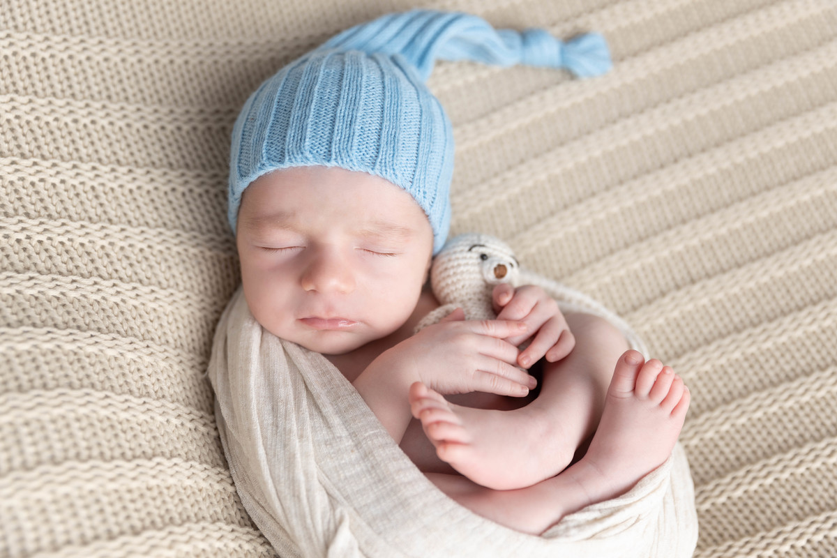 bebe deitado com mão no pezinho  no pufe com toquinha azul