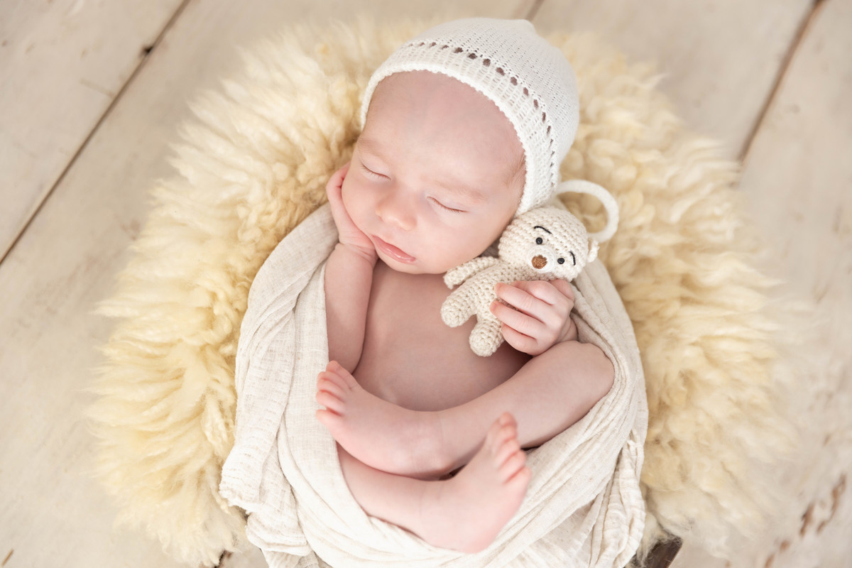 bebe deitado com mão no pézinho  no pufe com toquinha bege com ursinho