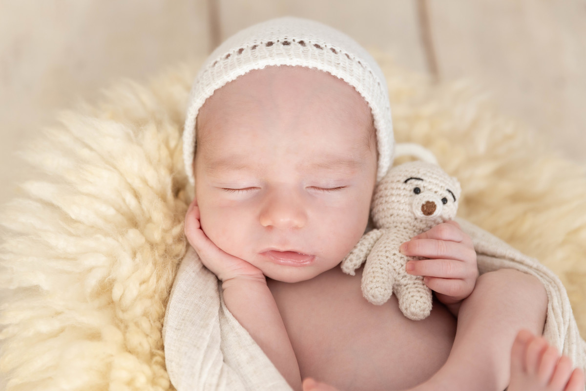 bebe deitado com mão no pézinho  no pufe com toquinha bege com ursinho