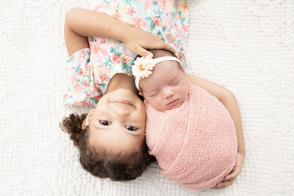 bebe enroladinha no braço da irmã