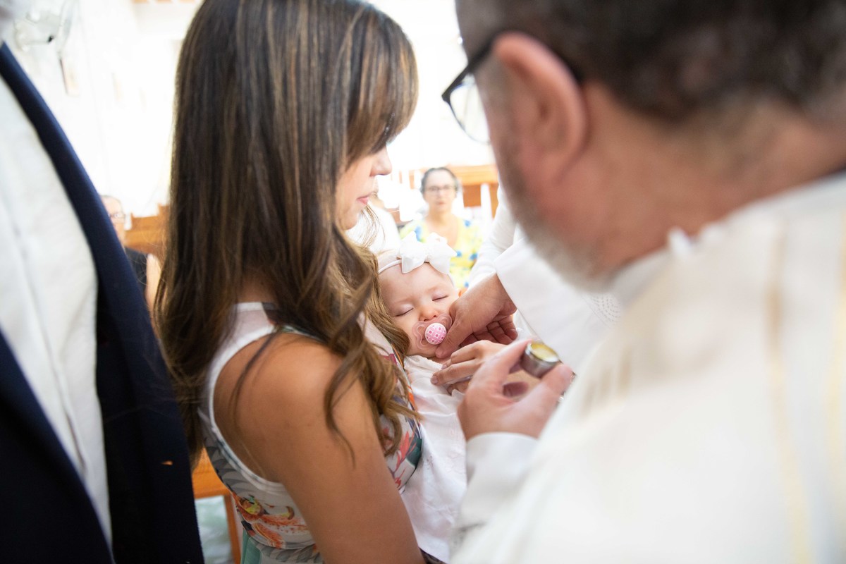 A madrinha segurando a Isabela para o padre ungir