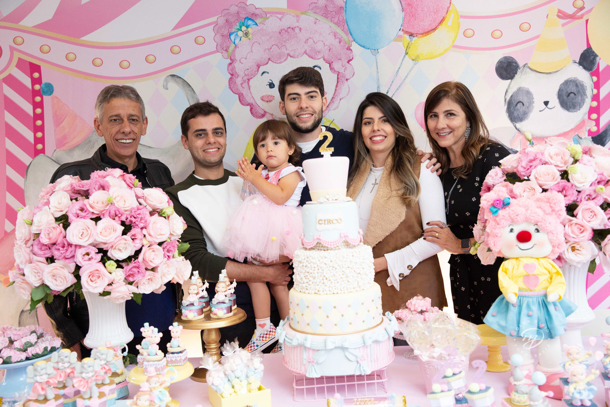 Festa infantil tema circo 2 anos menina rosa no colo dos tios com a família mesa do bolo