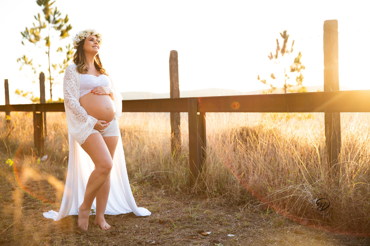 Gestante mamãe esperando bebe que irá nascer segurando barriga vestido branco roupa saia longa  pinheiros sereia coroa de flor cerca por do sol