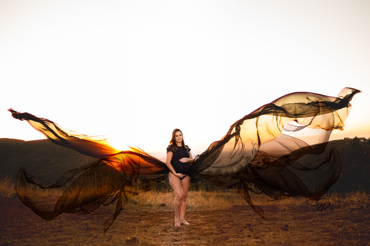 Gestante mamãe esperando bebe que irá nascer segurando barriga roupa preta body  por do sol tecido voando  por do sol