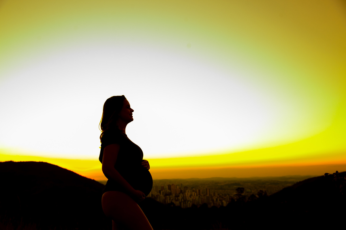 Gestante mamãe esperando bebe que irá nascer segurando barriga roupa preta body  por do sol tecido voando  por do sol silhoueta