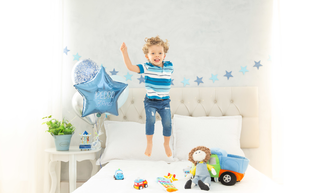 Menino lindo olhos azuis brinquedos carrinhos balões pulando cama