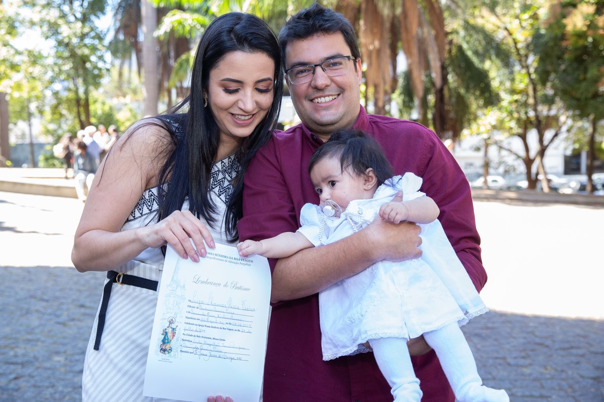 Luiza no colo dos pais com certificado de batismo