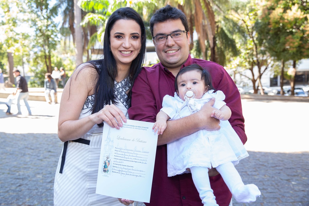 Luiza no colo dos pais com certificado de batismo