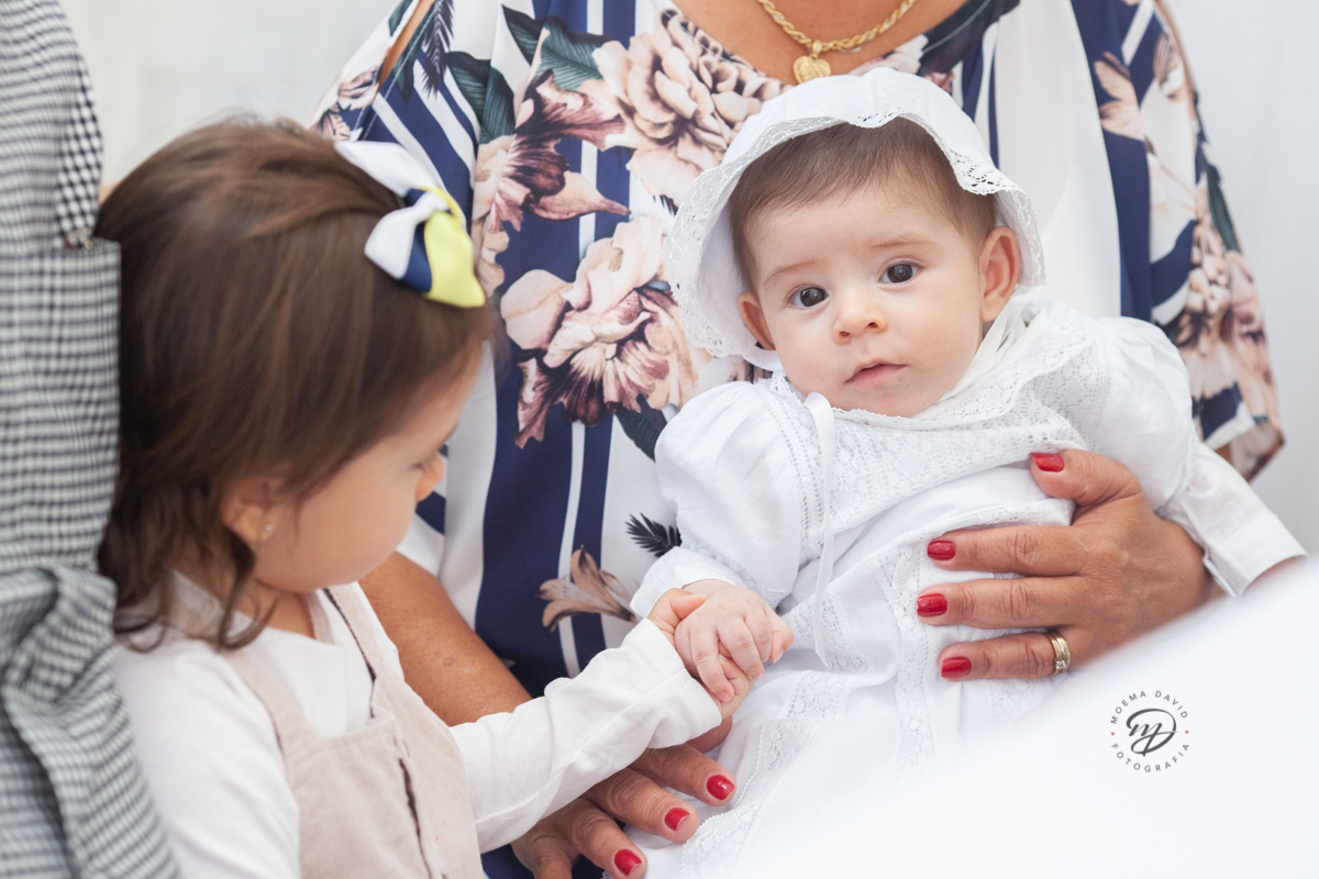 Irmã segurando a mão do irmãozinho no batizado, carinho