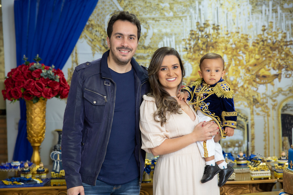 Príncipe Henrique no colo da mamãe e do papai com sua roupa de luxo