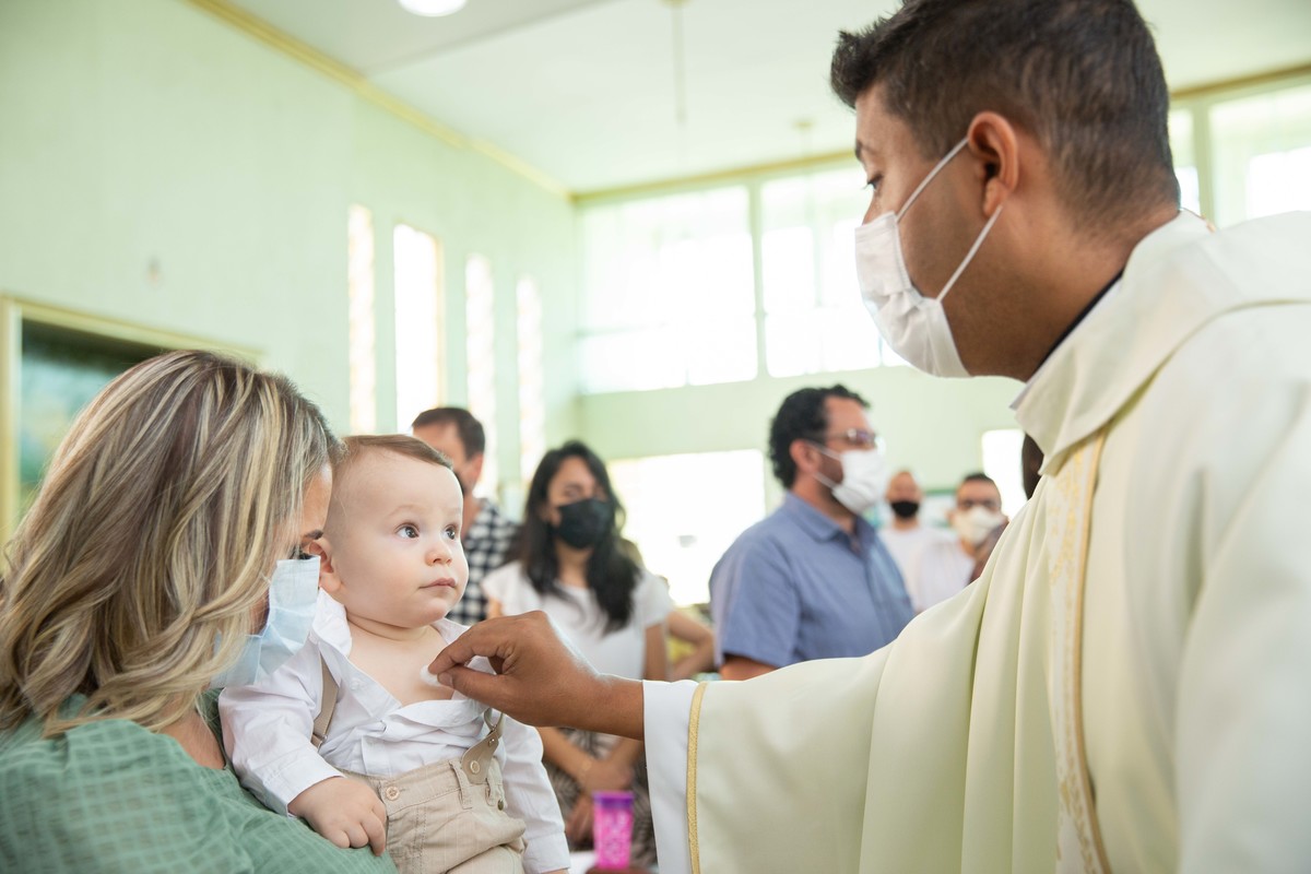 Menino olhando para o padre no colo da mae batizado unção com oleo no peito